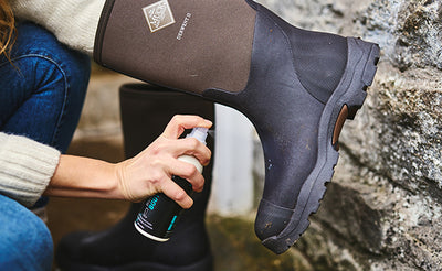 Person, die Grangers Gummistiefelpflegespray auf ein Paar Muck Boots Derwent II Gummistiefel aufträgt